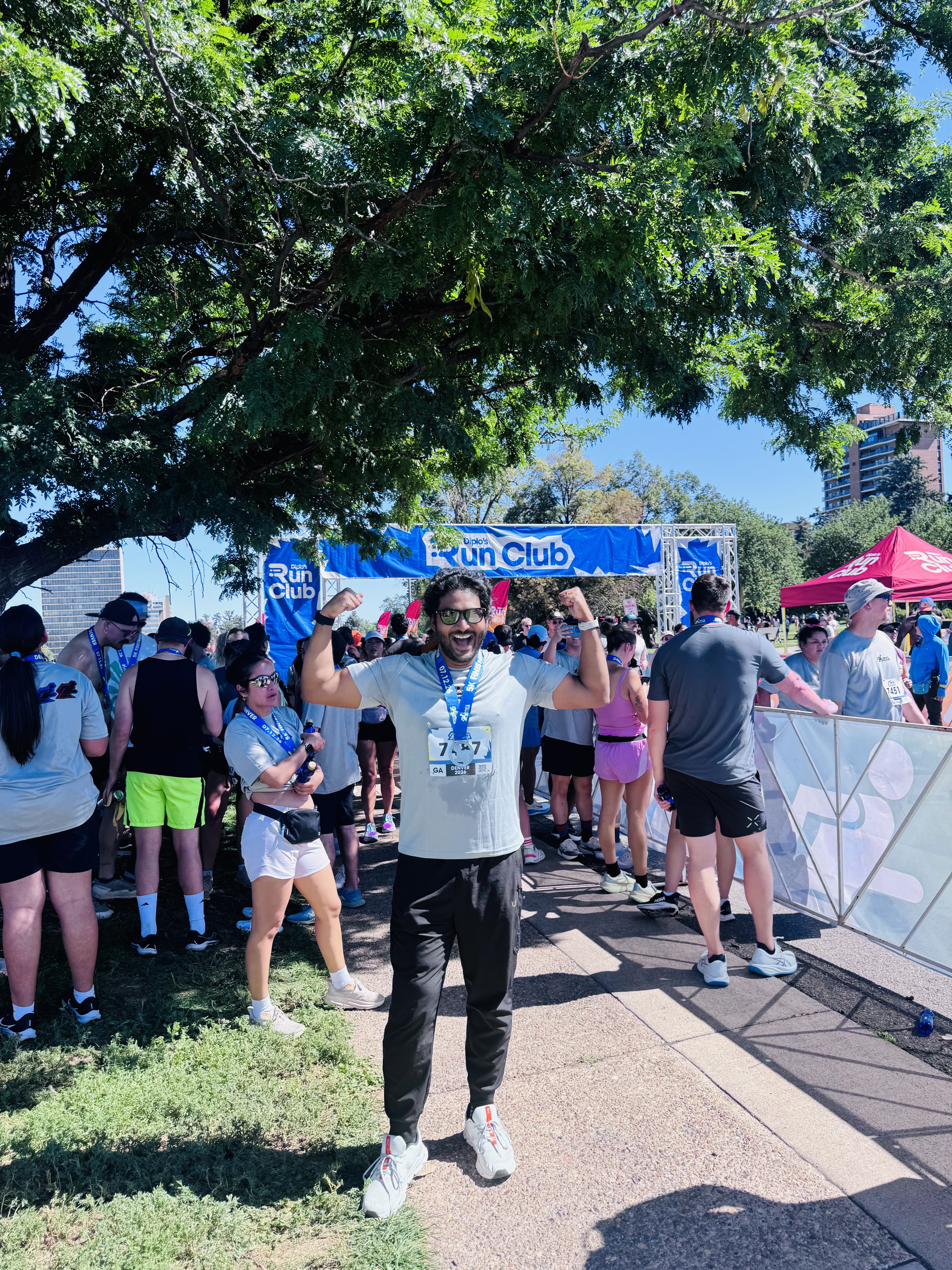 Teja celebrating with both arms raised at a 5K finish line in Denver.