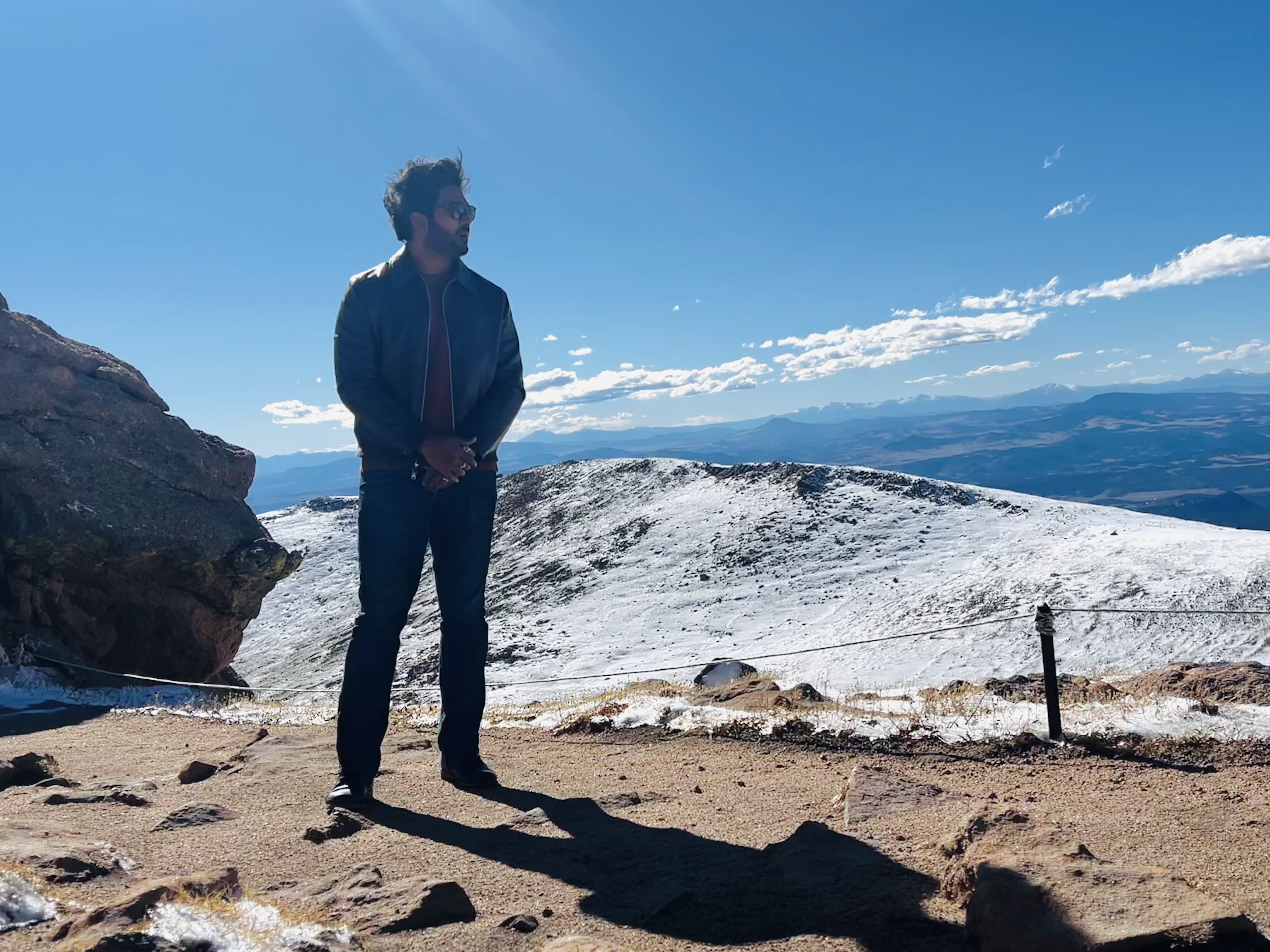 Teja standing on a snow-covered ridge in Colorado with mountains behind him.