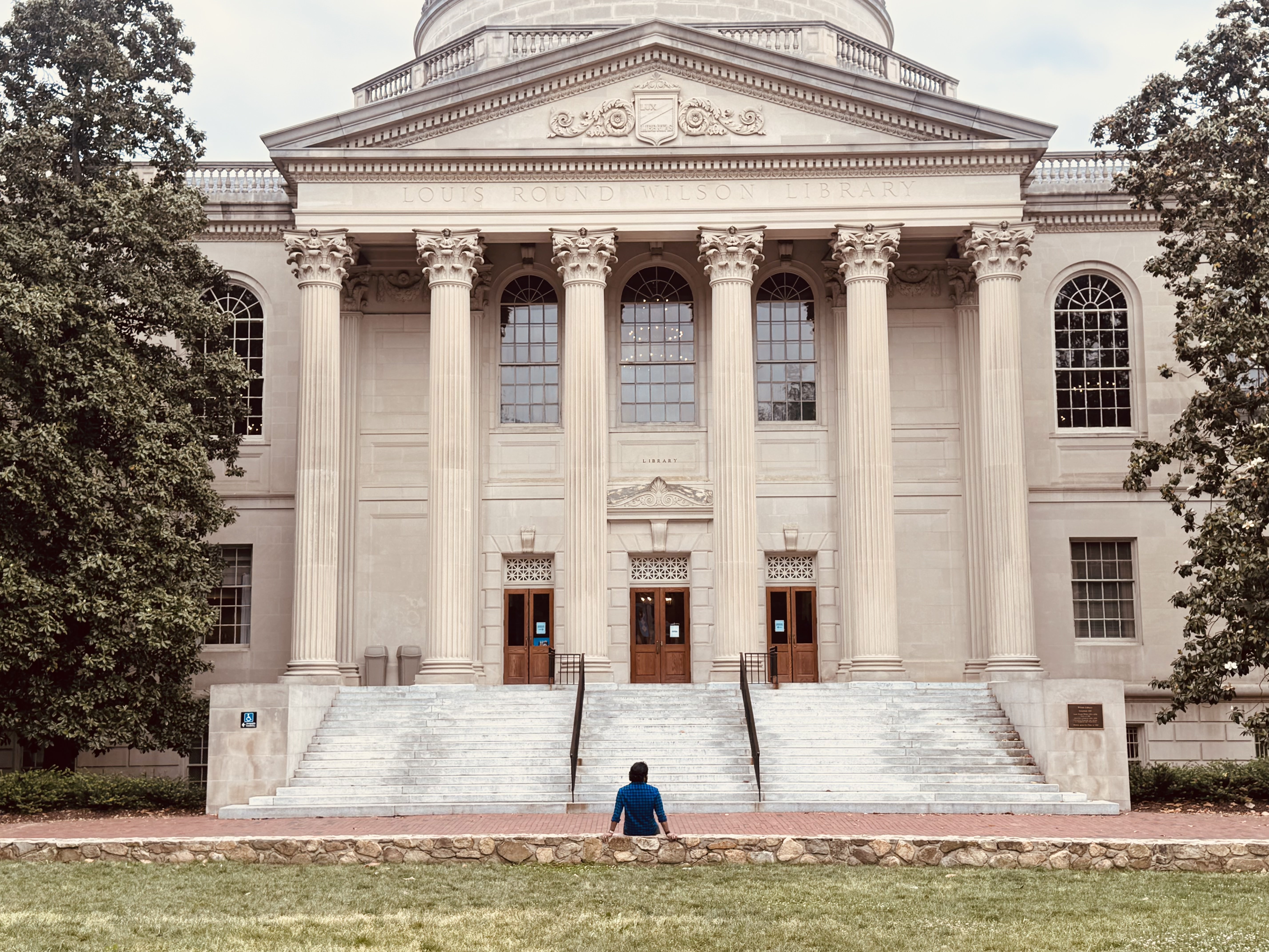 Teja seated on a low wall facing the columned façade of Louis Round Wilson Library at UNC.